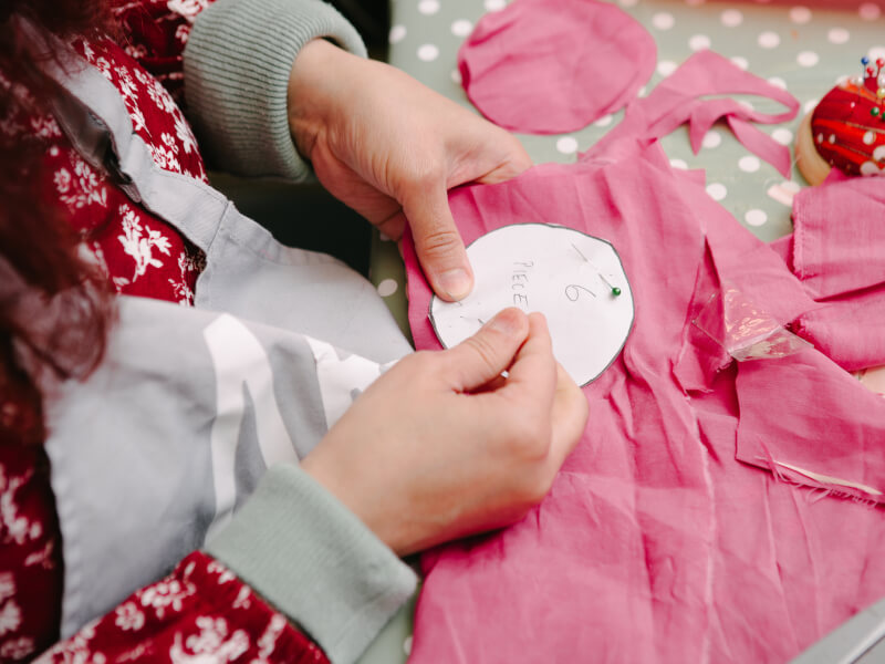 A close up of a person pinning a paper pattern to a piece of pink fabric